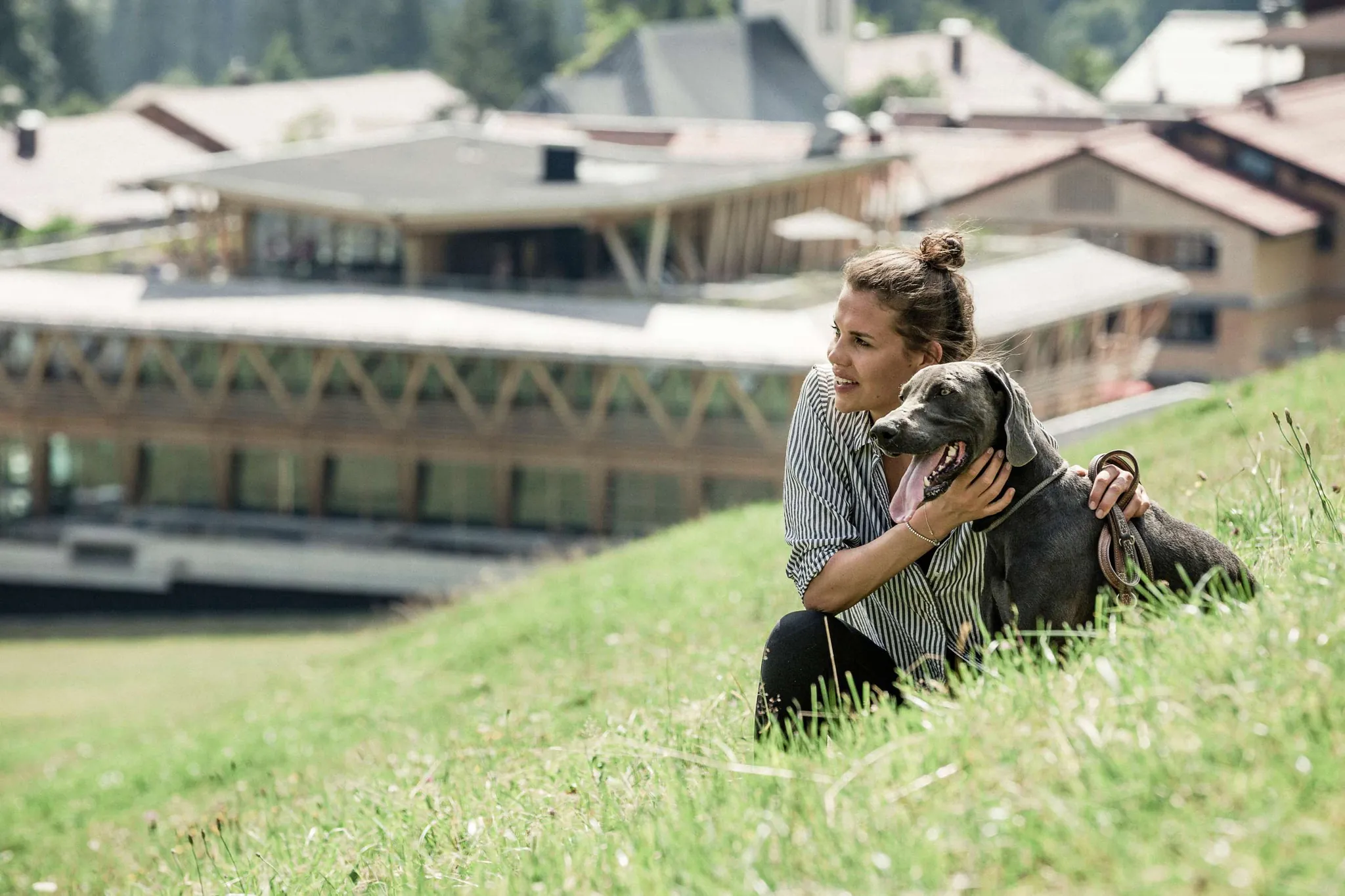 Eine Frau streichelt einen Hund auf einer Wiese vor dem Hundehotel HUBERTUS Mountain Refugio Allgäu sitzend