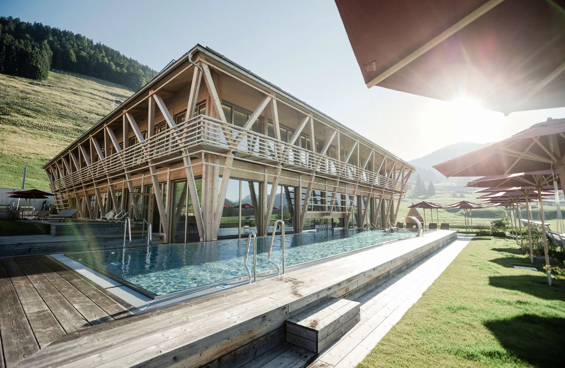 Außenansicht des Sporthotel HUBERTUS Mountain Refugio mit der aufsteigenden Sonne im Hintergrund