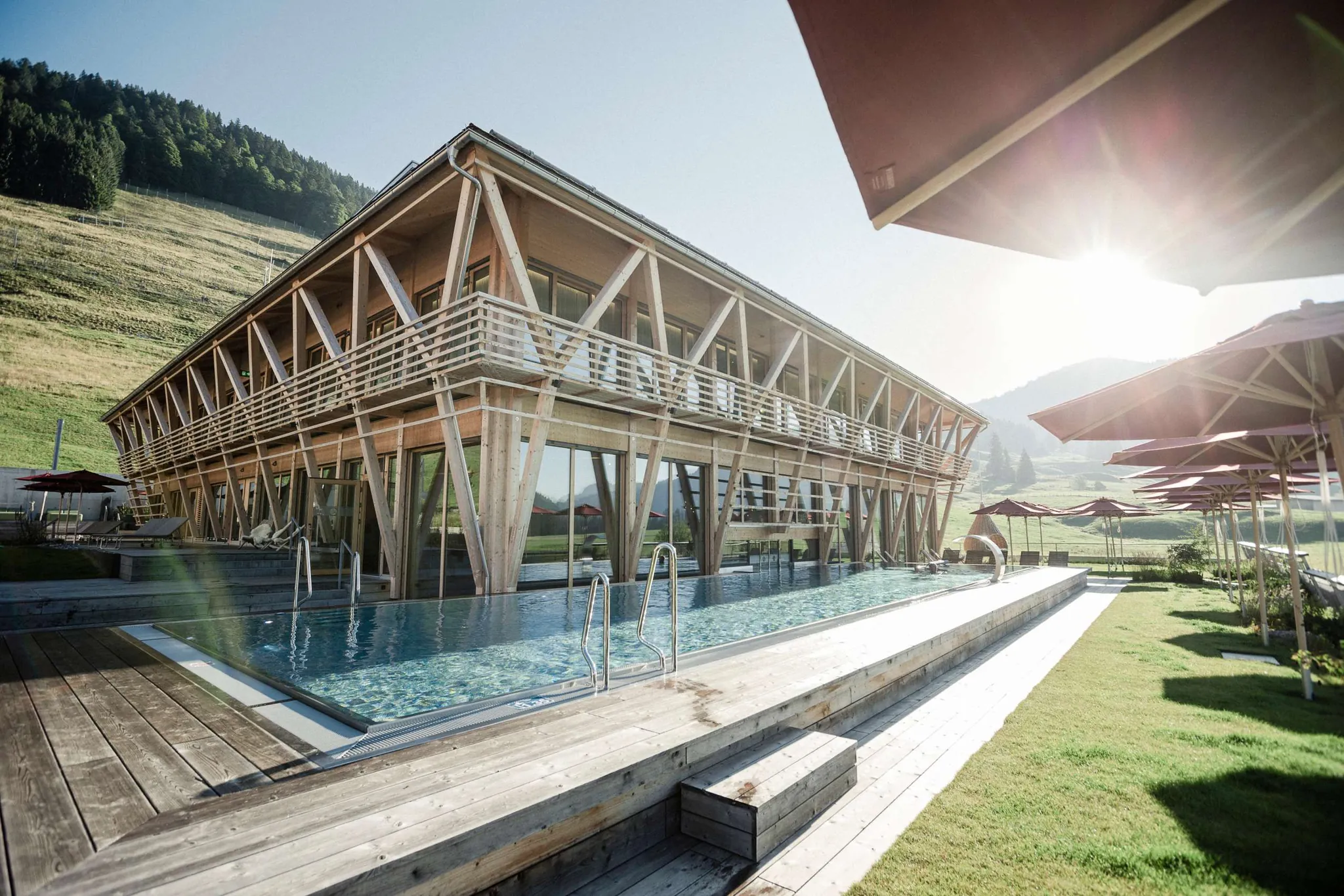 Außenansicht des Sporthotel HUBERTUS Mountain Refugio mit der aufsteigenden Sonne im Hintergrund