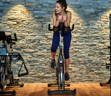 Frau beim Cycling im Fitnessbereich des Sporthotel HUBERTUS Mountain Refugio