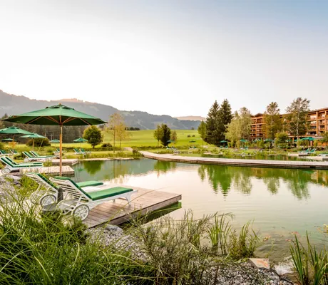 Blick auf den Außenbereich mit großem Badeteich und Liegen des Sporthotel Sonnenalp Resort