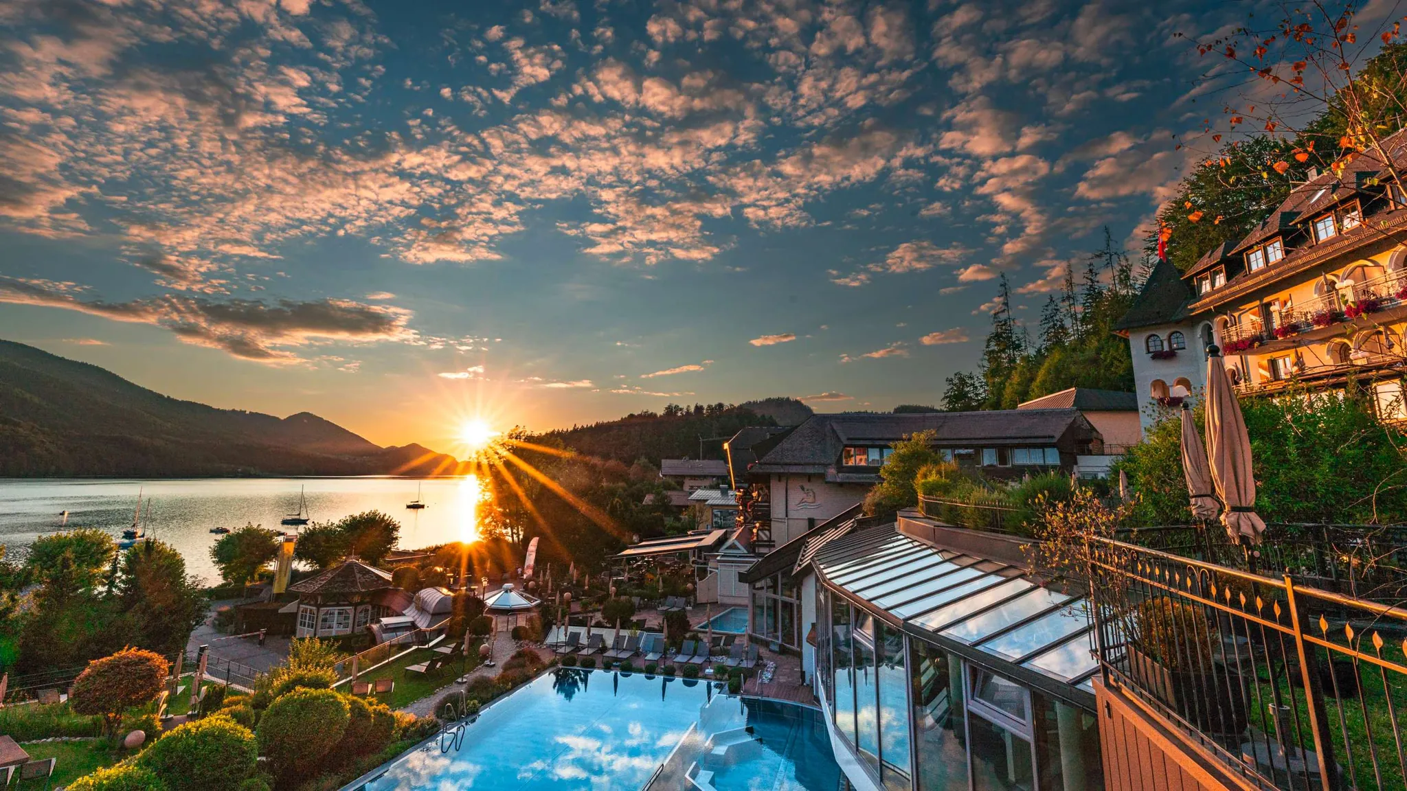 Außenansicht des Wellnesshotel Ebner’s Waldhof am See Alpines Spa und Golf Resort. Im Hintergrund geht die Sonne unter