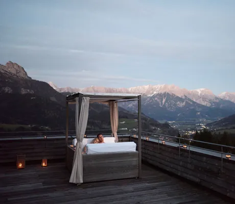 Eine Frau und ein Mann liegen auf einem Bett auf der Dachterrasse des Sporthotel Rooftophotel Forsthofalm