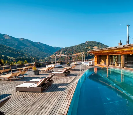 Pool des Sporthotel Rooftophotel Forsthofalm auf dem Dach. Davor stehen Liegestühle