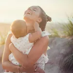 Junge Frau am Strand mit Baby auf dem Arm