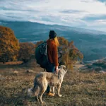 Frau mit weißen Hund blickt über die Berge