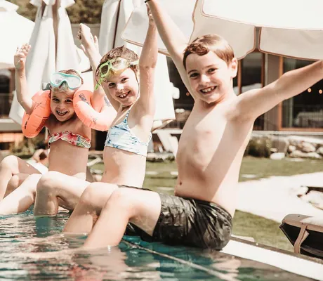 drei Kinder sitzen am Pool und freuen sich_Feuerstein_Gossensass