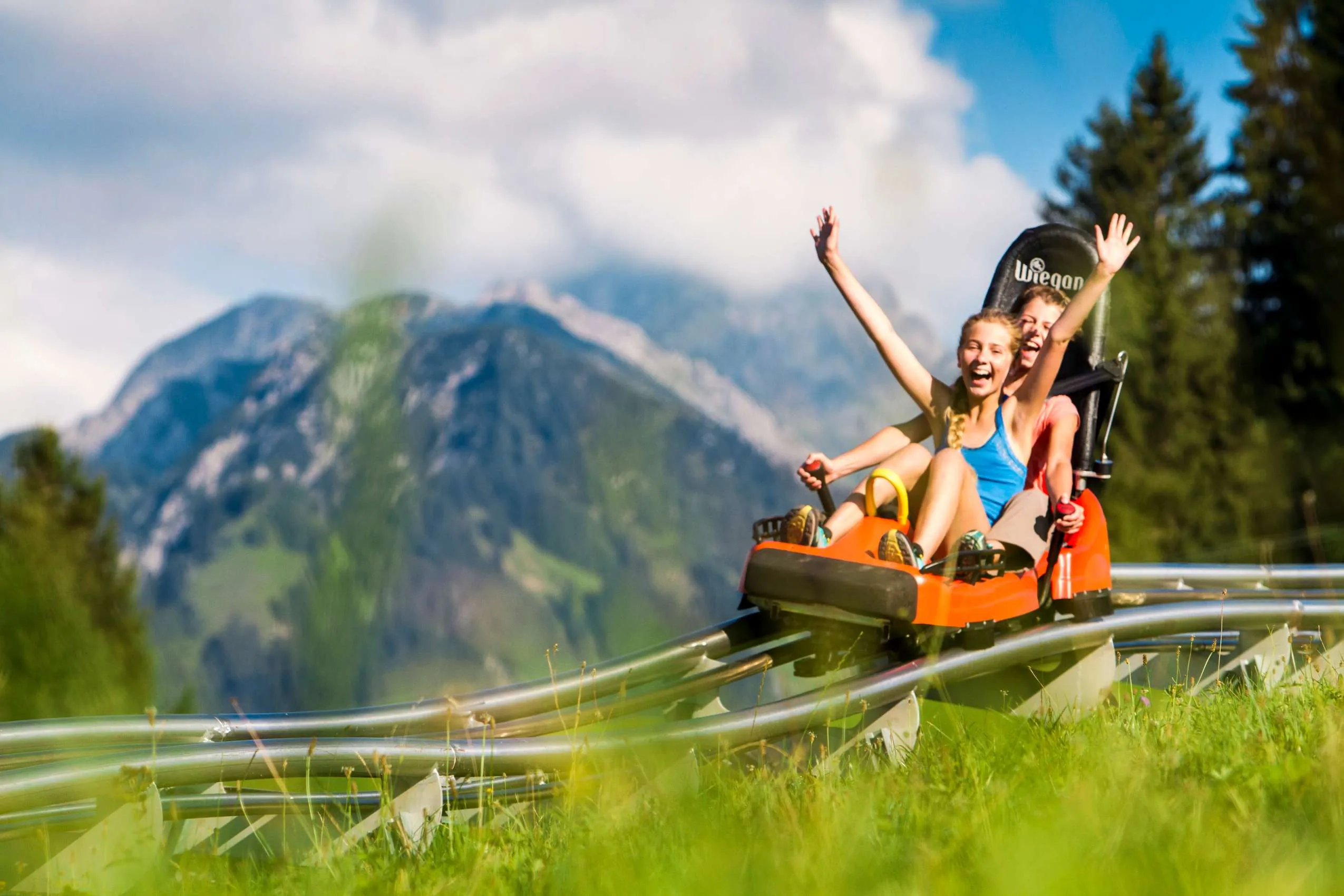 Zwei Kinder fahren eine Sommerrodelbahn im Allgäu und lachen