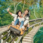 Junges Paar fährt einen Bob im Alpsee Coaster, Frau winkt