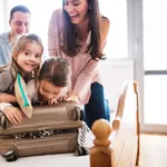 Mama, Papa und zwei Kinder packen fröhlich den Urlaubskoffer für den Familienurlaub