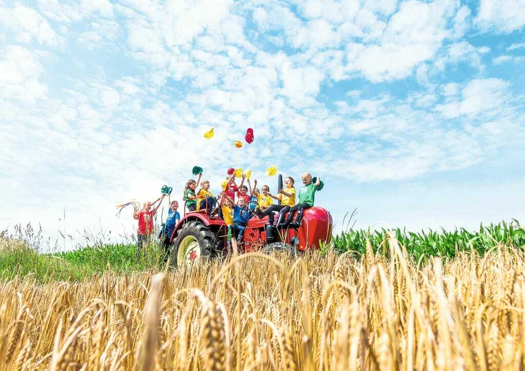 Kinder sitzen auf einem Trecker umgeben von Feldern.