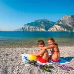 Gardaseeurlaub mit Kindern, die auf dem Kiesstrand am See sitzen.