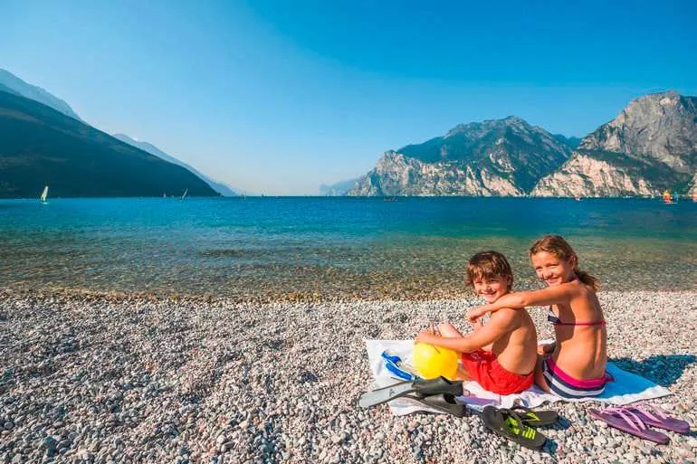 Gardaseeurlaub mit Kindern, die auf dem Kiesstrand am See sitzen.