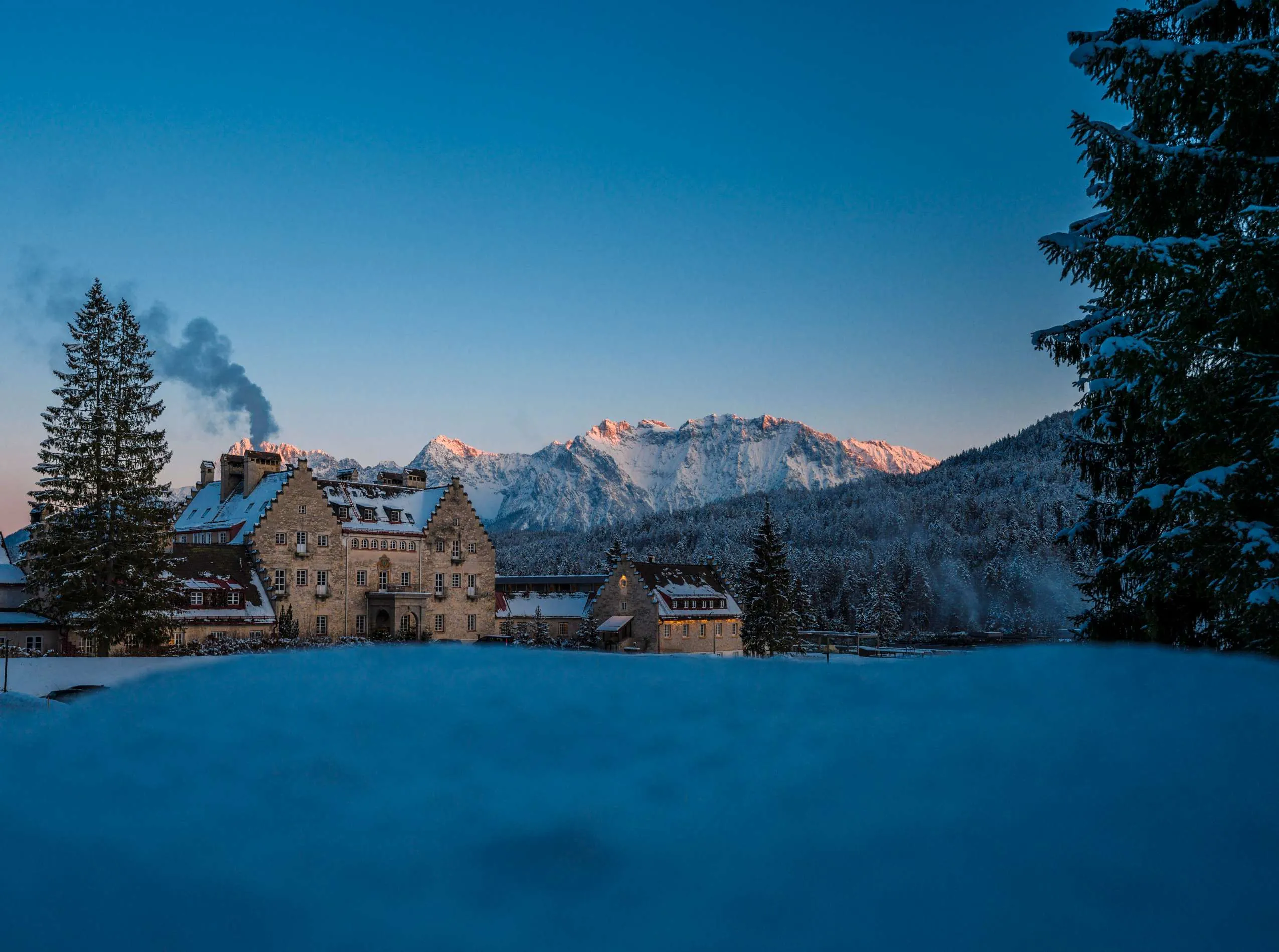 Au&szlig;enansicht des Wellnesshotels DAS KRANZBACH mit einem verschneiten Wald und Bergen im Hintergrund.