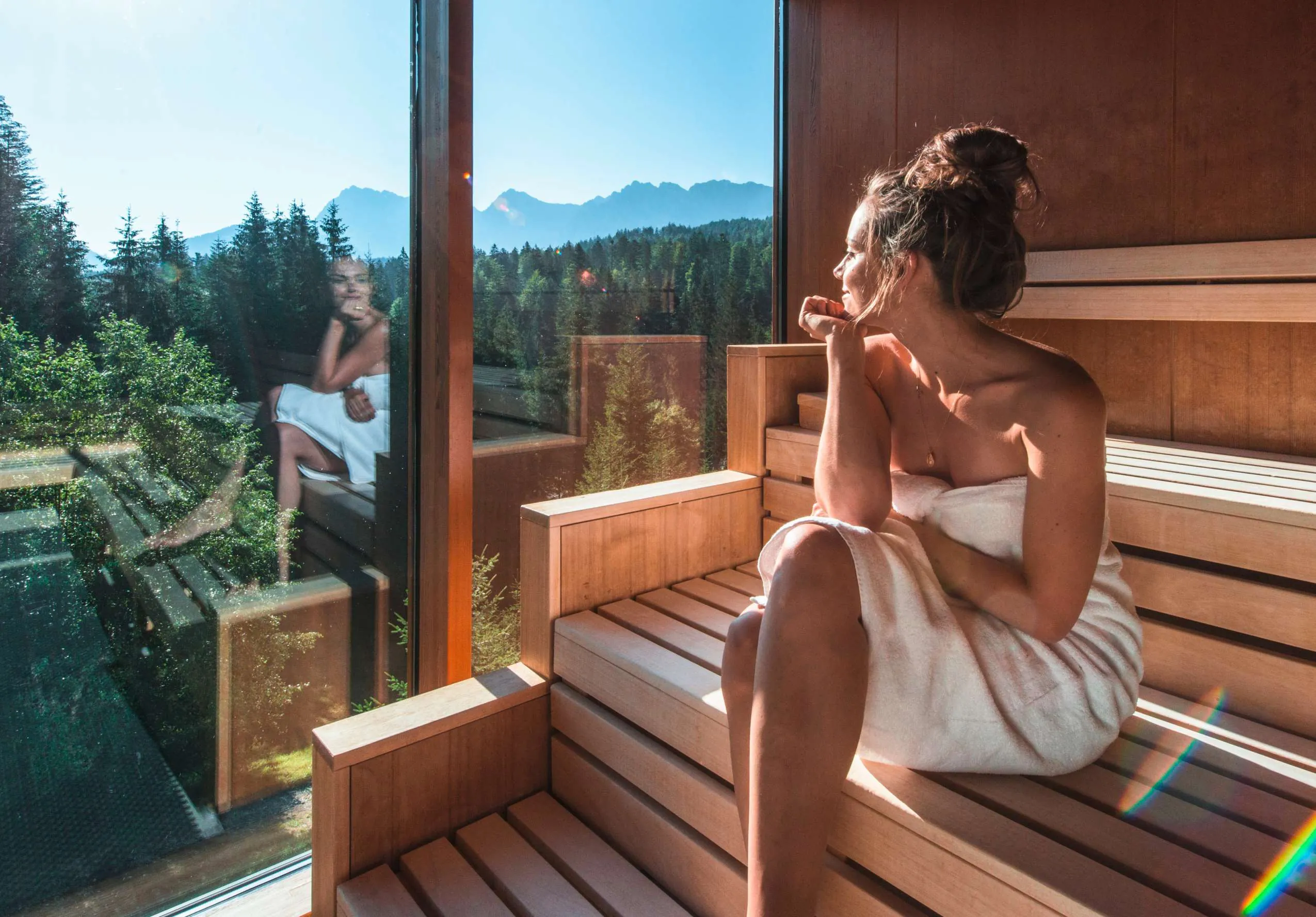 Frau Sitz in der Sauna und schaut aus dem Fenster im Wellnesshotel das Kranzbach.