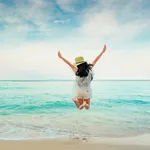 Junge Frau springt am Strand in die Luft