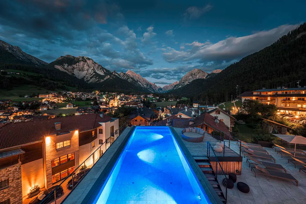 Panorama-Infinity-Pool im Excelsior Dolomites Life Resort in Südtirol mit nächtlicher Beleuchtung