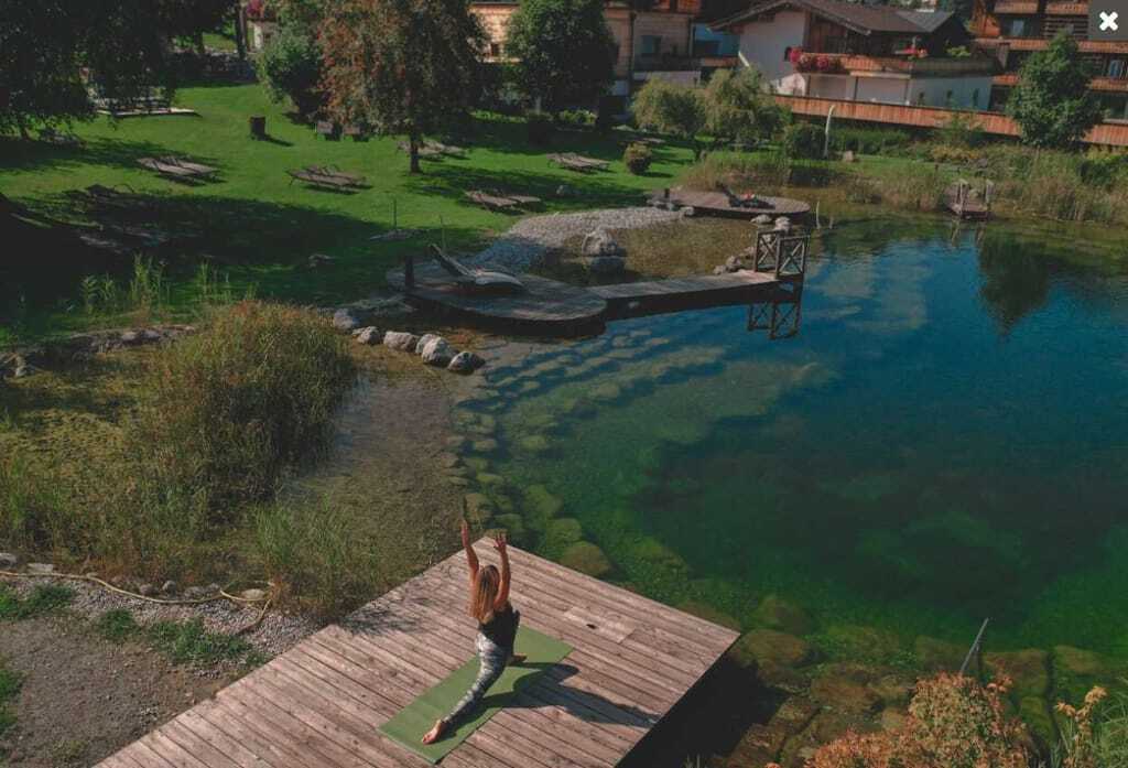 Frau, die vor Teich und Häusern Yoga macht