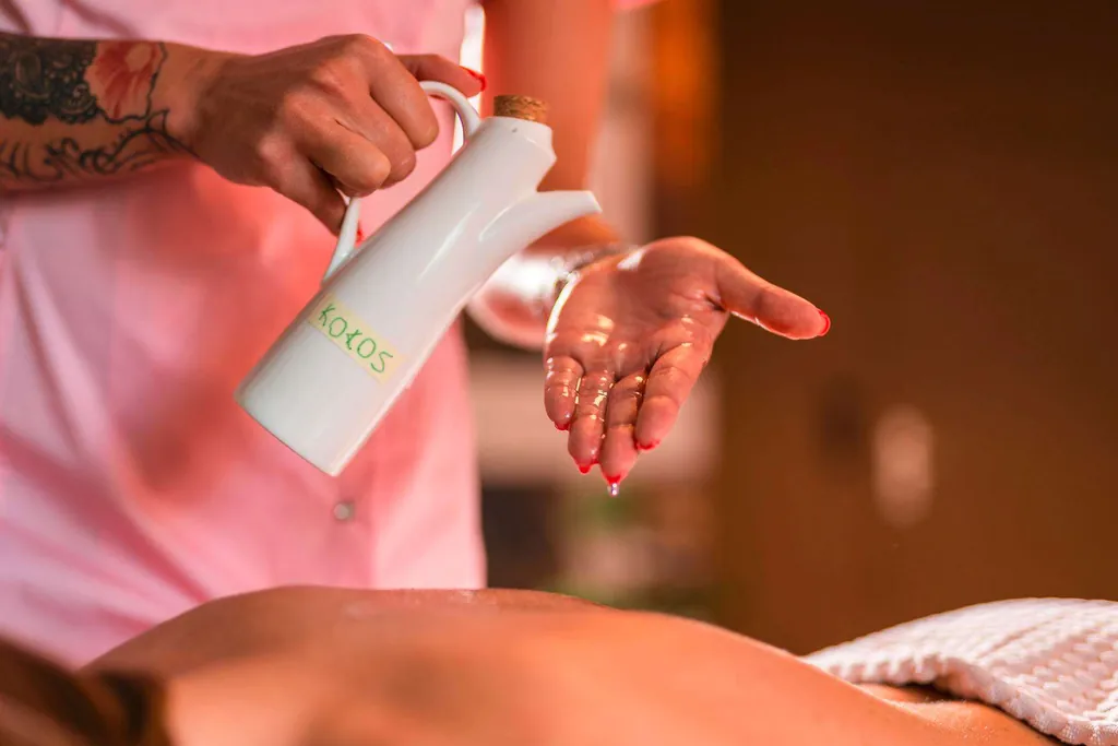 Masseurin verteilt Öl auf Rücken einer Frau für Aromamassage