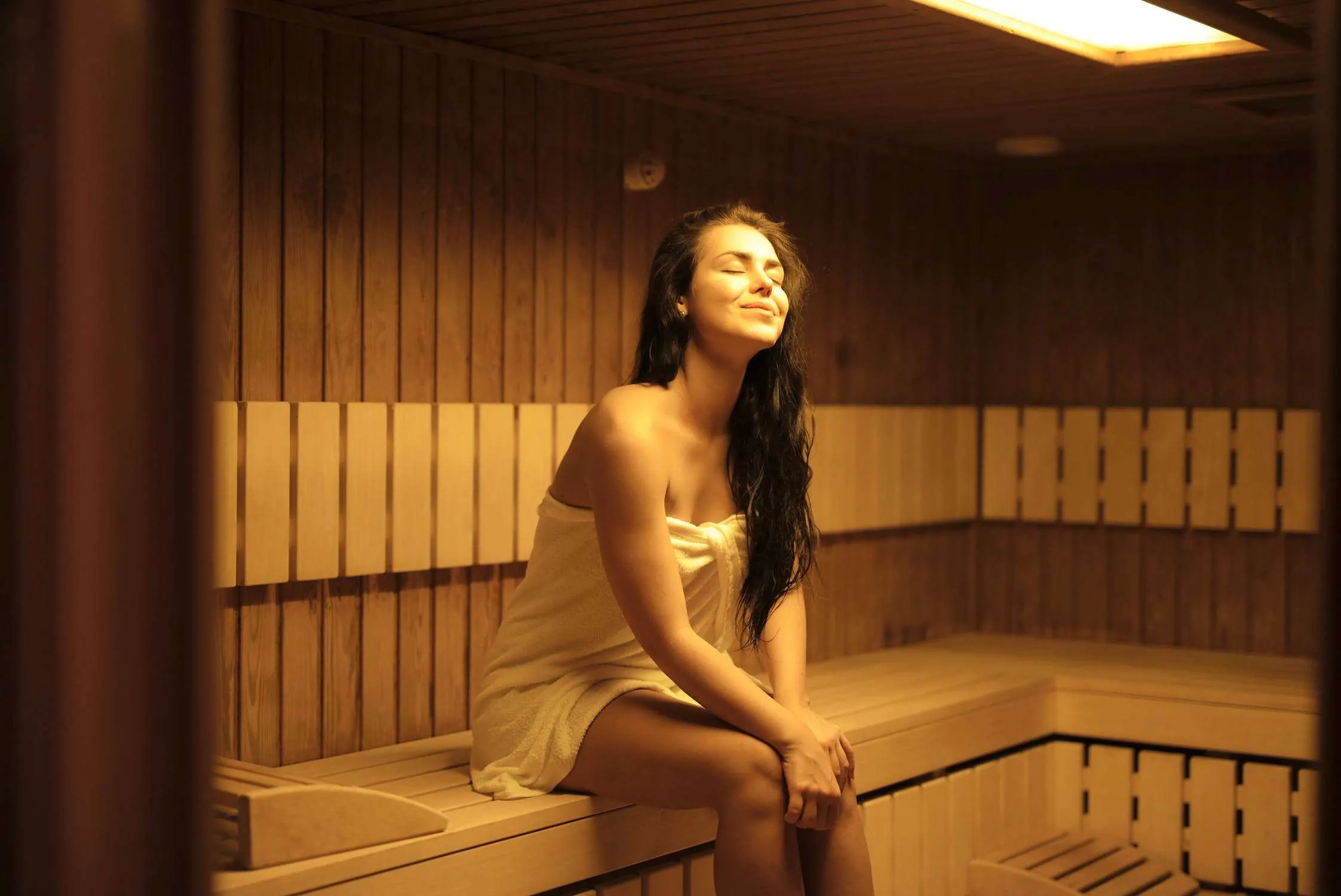 Junge Frau mit Handtuch sitzt in Biosauna mit gelbem Licht