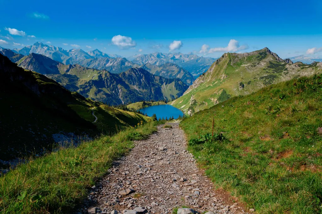 Schmaler Wanderweg zu einem Bergsee mit Bergen im Hintergrund