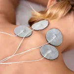 Rückenansicht einer jungen Frau mit aufgeklebten Elektroden im Rahmen einer Elektrotherapie