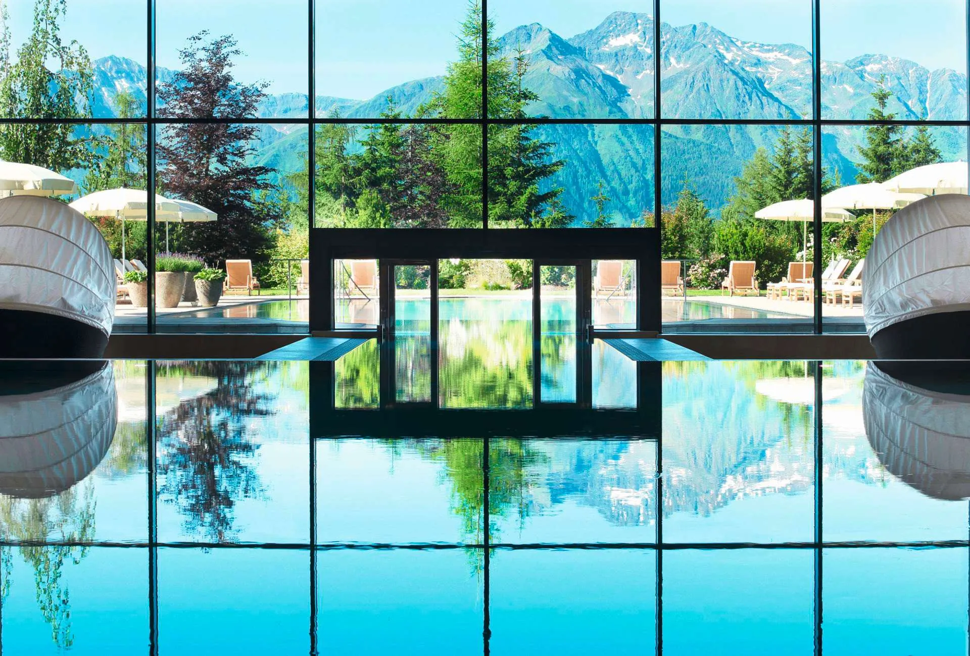spiegelglatter Indoorpool mit Schleuse zum Outdoorpool und Blick auf die Berge