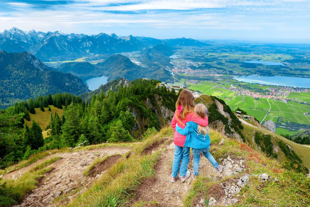 Zwei junge Mädchen stehen auf Aussichtspunkt am Berg und blicken aufs Allgäu