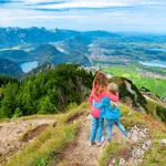 Zwei junge Mädchen stehen auf Aussichtspunkt am Berg und blicken aufs Allgäu