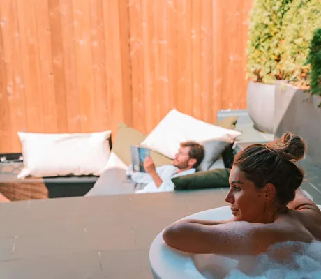 Frau in Badewanne schaut auf Mann im Liegenetz, der Zeitung liest