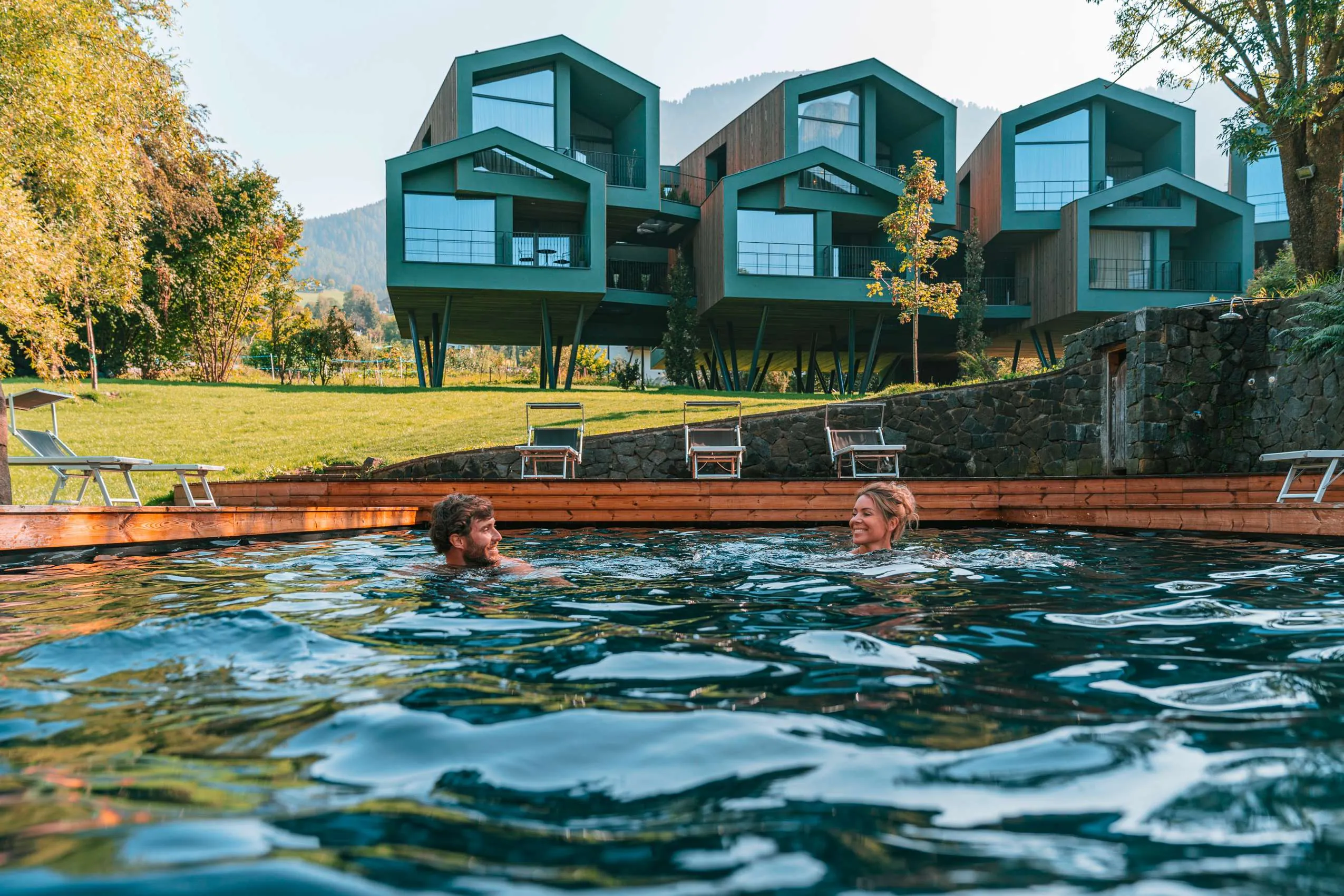 Paar schwimmt im Outdoorpool vor Chaltets auf Stützen im Hintergrund