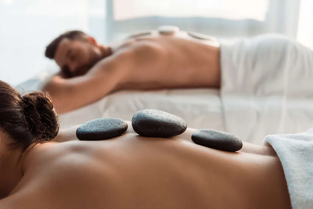 Drei schwarze, rundlicher Steine liegen während einer Hot-Stone-Massage auf dem Rücken einer Frau und eines Mannes