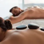 Paar erhält Hot-Stone-Massage, auf dem Rücken liegen schwarze, rundliche Basaltsteine