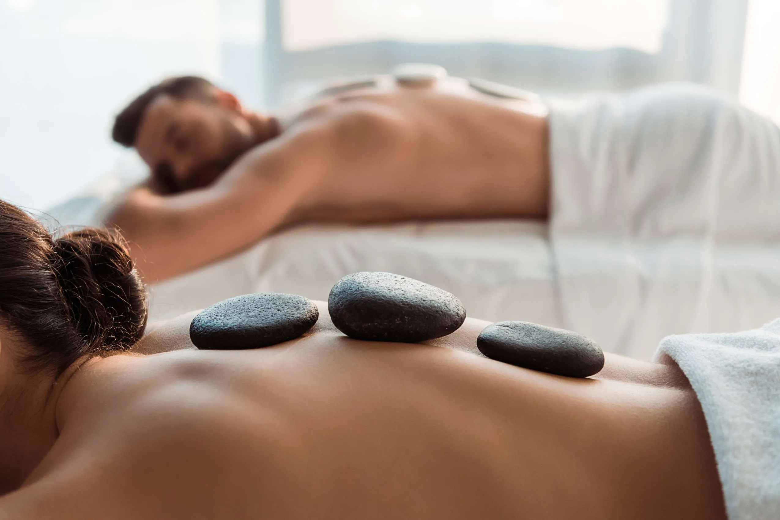 Paar erhält Hot-Stone-Massage, auf dem Rücken liegen schwarze, rundliche Basaltsteine
