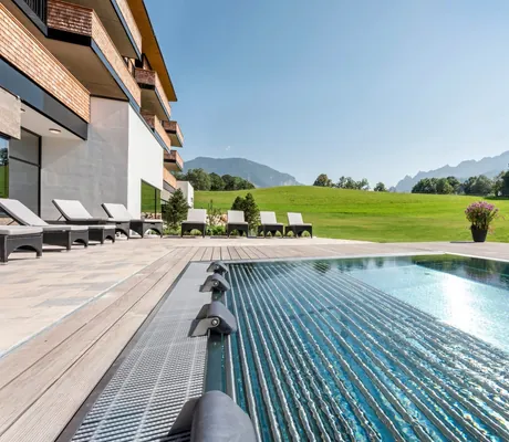 Außenpool in der Sonne mit Wiese, Bäumen und Bergen im Hintergrund