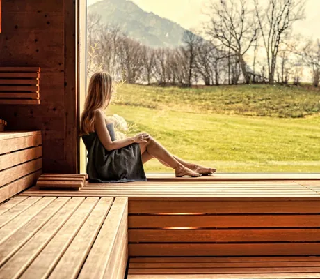 Frau sitzt in Sauna und schaut nach draußen in die Natur