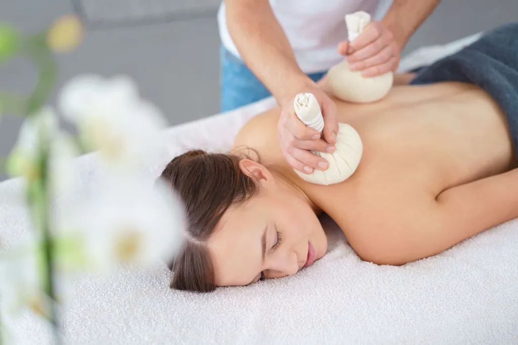 Therapeut massiert eine Frau mit Kräuterstempeln