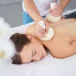 Therapeut massiert eine Frau mit Kräuterstempeln