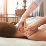 Mann liegt bei einer Massage-Behandlung auf dem Bauch und wird an den Schultern massiert