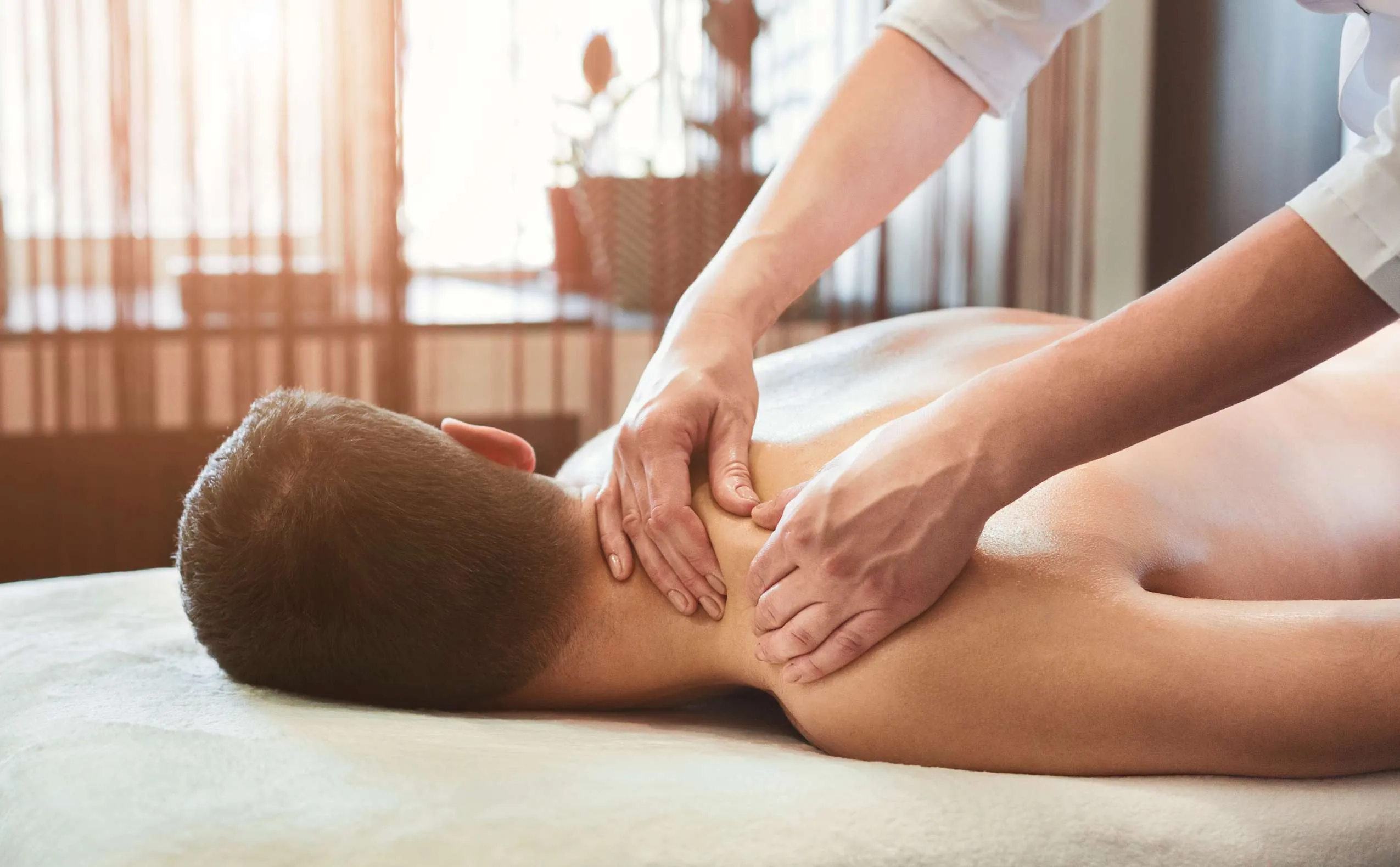 Mann liegt bei einer Massage-Behandlung auf dem Bauch und wird an den Schultern massiert