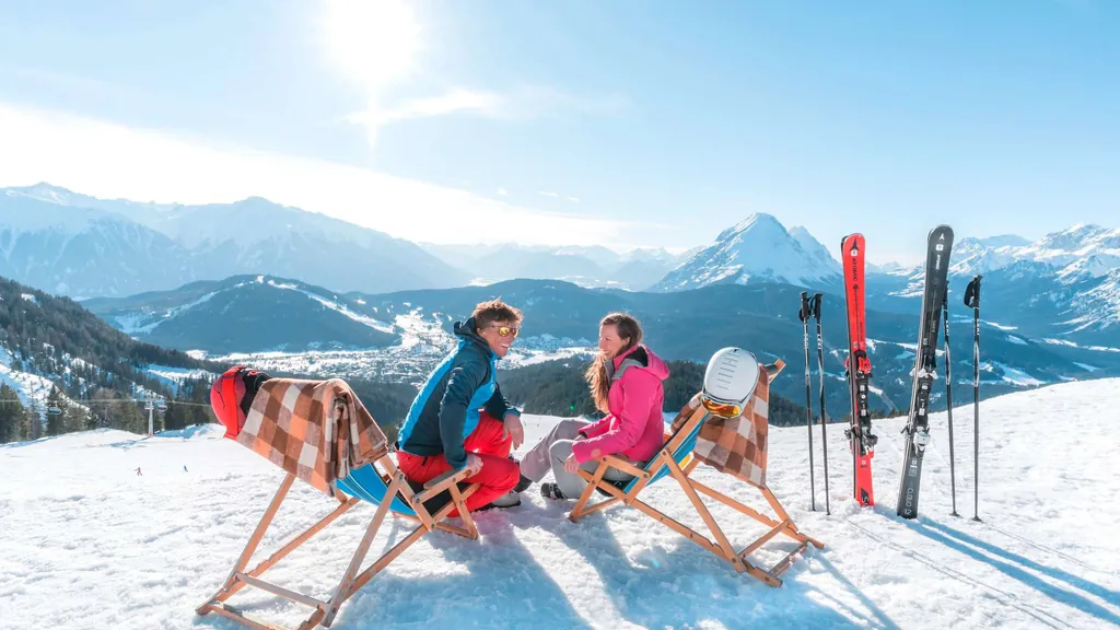Zwei Skifahrer sitzen in Liegest&uuml;hlen und blicken auf die Skiregion Seefeld in Tirol