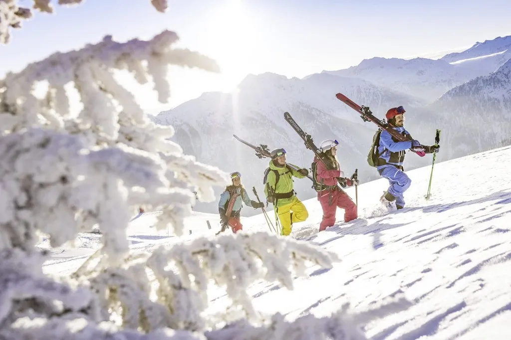 Vier Skifahrer haben ihre Ski auf den Schultern und laufen einen schneebedeckten Berg hoch unweit des Sporthotel Sonnberg Ferienanlage in &Ouml;sterreich