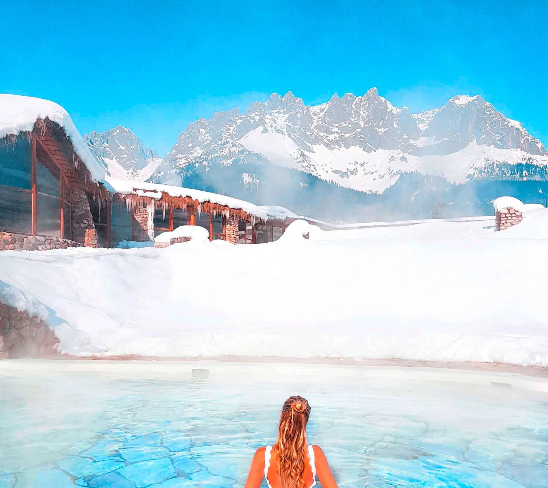 Frau steht in schneebedeckter Umgebung im Au&szlig;enpool des Sporthotels Bio- und Wellnessresort Stanglwirt