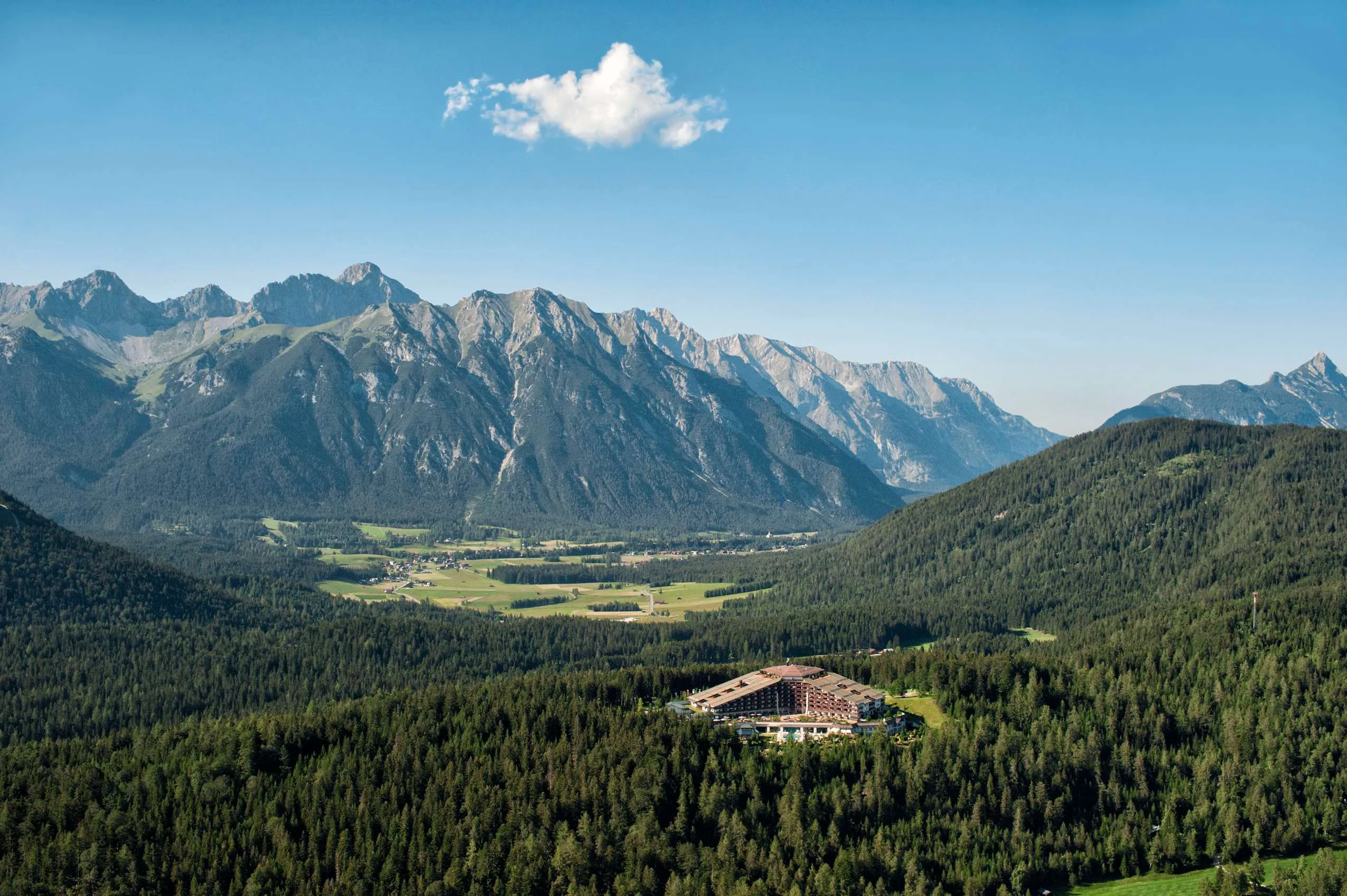 Luftaufnahme des Sporthotels Interalpen Hotel. Umgeben von W&auml;ldern und einer Bergkette im Hintergrund