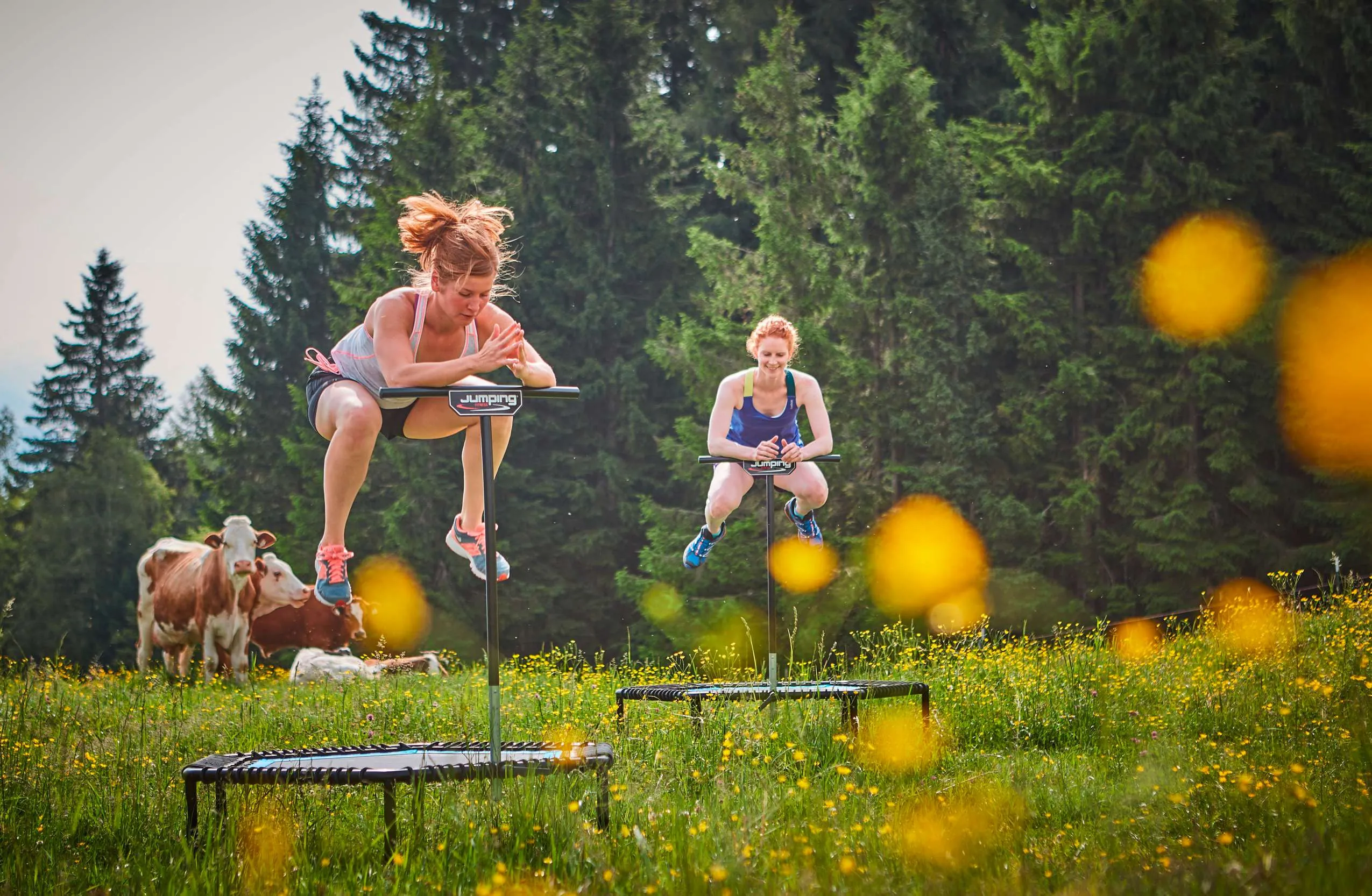 Zwei Frauen betreiben drau&szlig;en jumping und im Hintergrund stehen K&uuml;he
