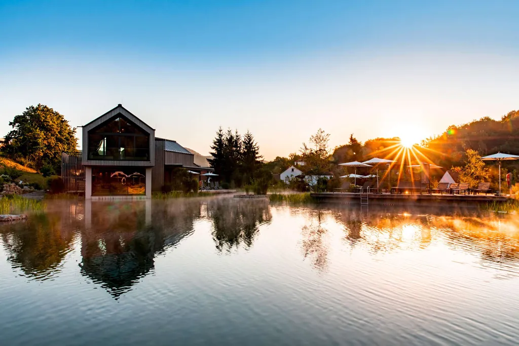 Blick auf das Weinhotel Pfalzblick Wald Spa Resort mit Naturbadeteich im Vordergrund