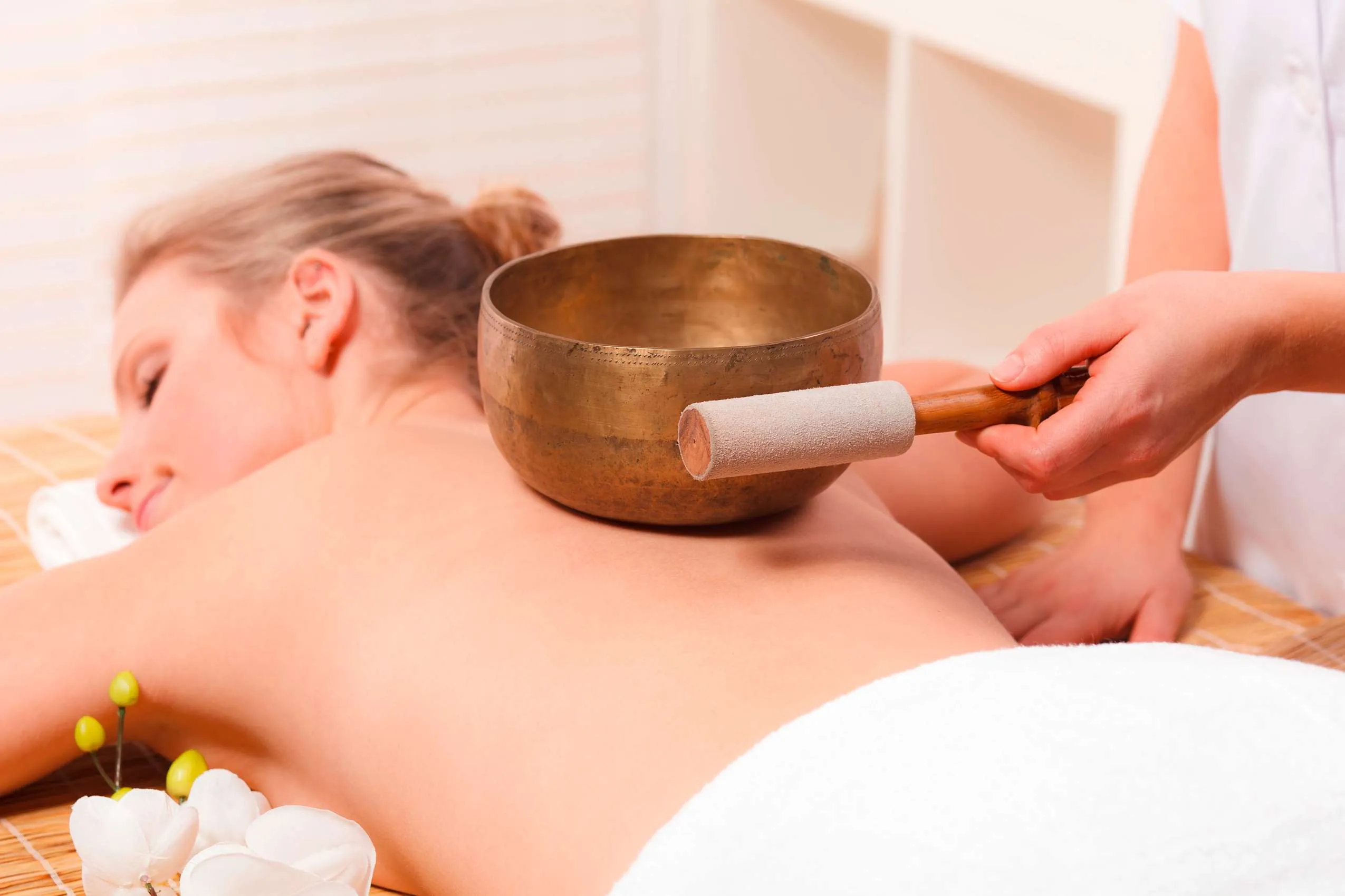 Frau liegt auf einer Liege und genießt eine Klangschalenmassage