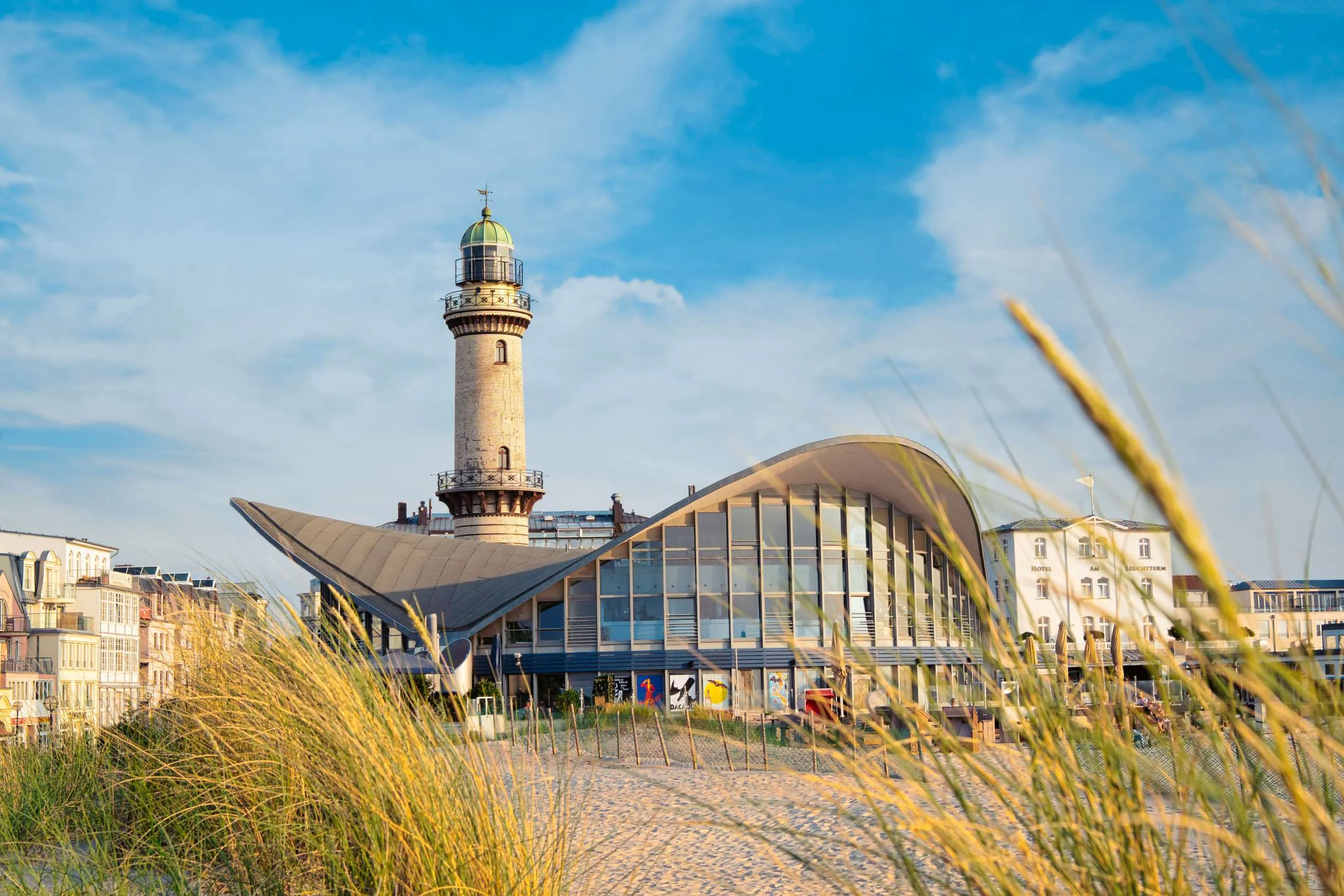 Ein Blick von den D&uuml;nen auf das Restaurant Teepott und den Leuchtturm im Stadtteil Warnem&uuml;nde in Rostock bei einem St&auml;dtetrip in Deutschland