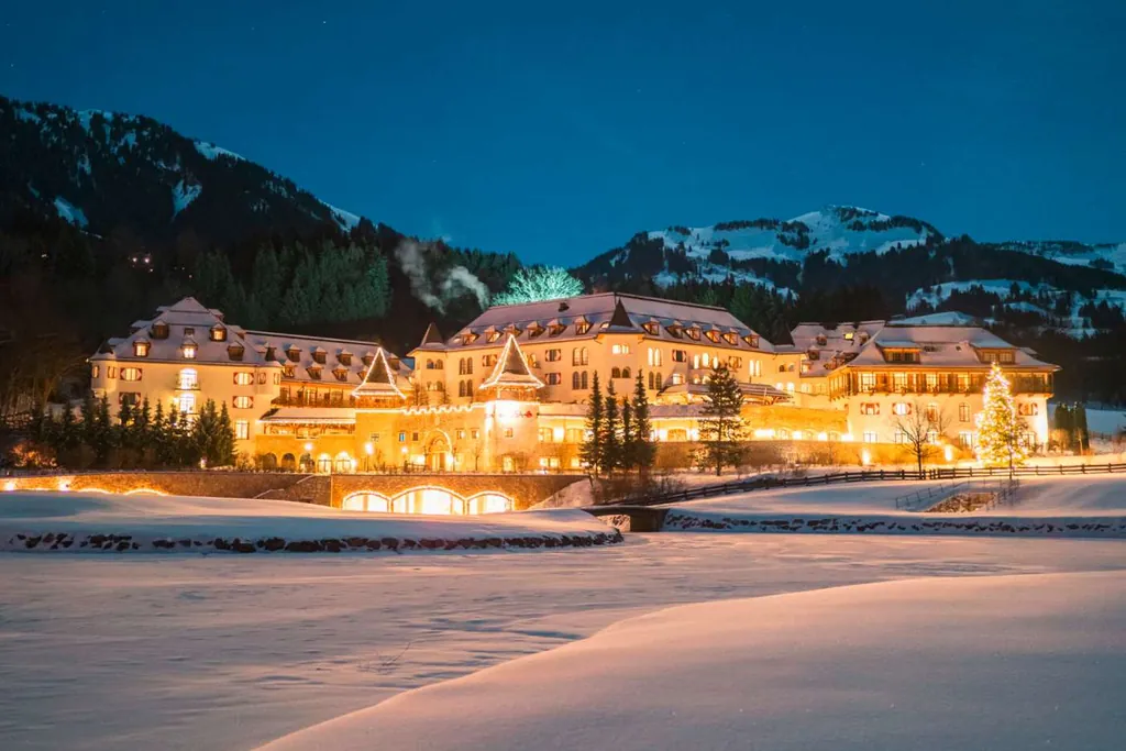 Aus der winterlichen Landschaft sticht das leuchtende Sport- und Wellnesshotel A-ROSA Kitzbühel aus der Nacht heraus
