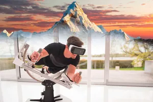 Ein Mann, der eine Virtual-Reality-Brille auf dem Gesicht hat liegt auf einem Simulator-Stuhl. Im Hintergrund zeichnet sich ein Berg ab